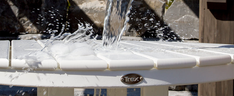 Water pours from a green bucket onto a round white Trex Outdoor Furniture dining table.
