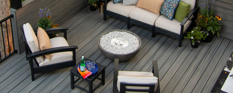 Assorted black Trex Outdoor Furniture Rockport deep seating and tables with white cushions sit on a grey deck balcony.