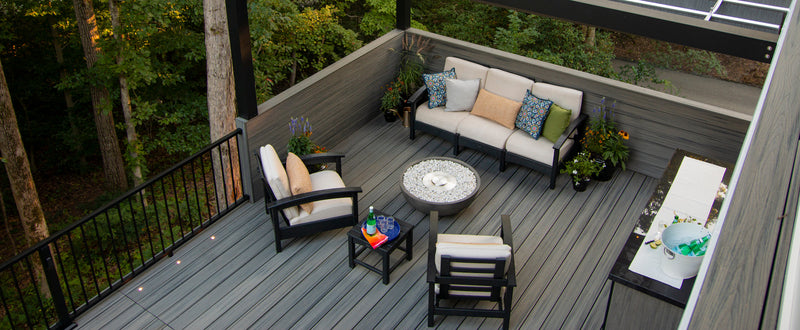 Assorted black Trex Outdoor Furniture Rockport deep seating and tables with white cushions sit on a grey deck balcony.