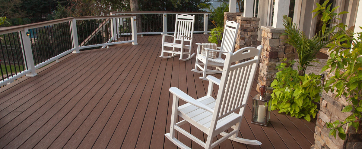 Three white Trex Outdoor Furniture Yacht Club Rocking Chairs sit before stone pillars on a covered deck with potted plants.