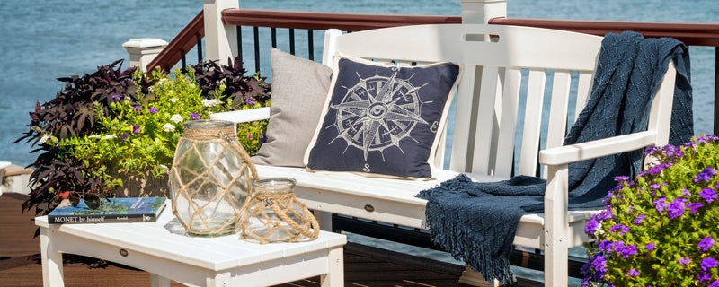 A white Trex Outdoor Furniture Yacht Club 60 Inch Bench with nautical decor and potted plants sits on a waterfront deck.