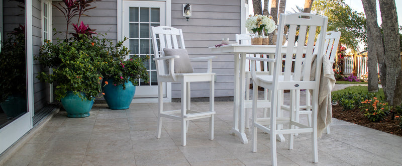 White Trex Outdoor Furniture Yacht Club Bar Arm Chairs and a Farmhouse Trestle 37 Inch Bar Table sit on a tile patio.