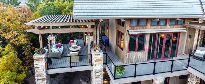 An elevated deck with a pergola features outdoor seating around a fire table, attached to a house with red trim.