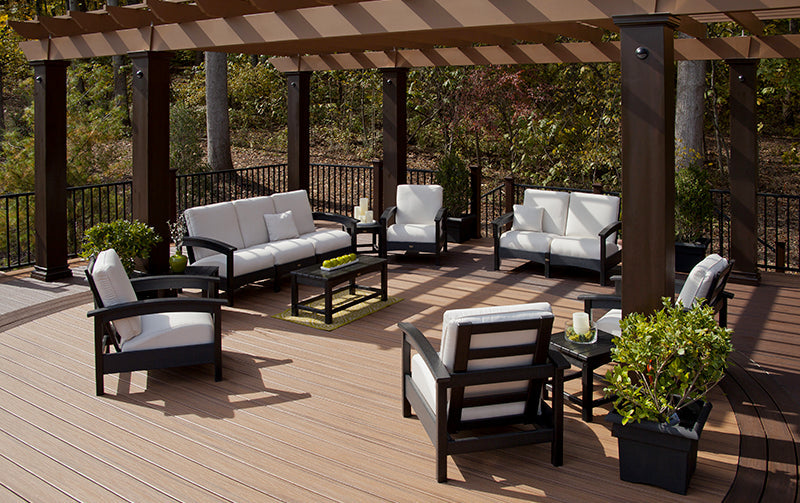 Assorted black deep seating pieces from Trex Outdoor Furniture Rockport Collection are arranged on a deck under a pergola.