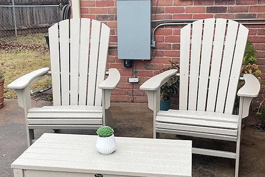 Two white Trex Outdoor Furniture Yacht Club Curveback Adirondack Chairs sit before a brick house.