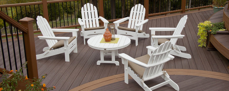 A white Trex Outdoor Furniture Cape Cod 6 Piece Folding Adirondack Conversation Set sits on a brown composite deck.