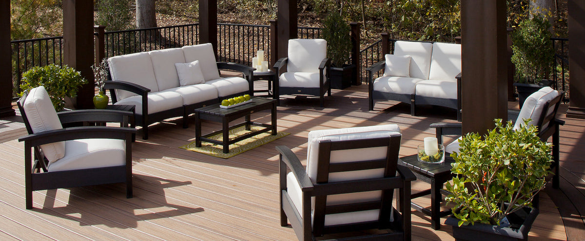 Assorted seating and tables from the Trex Outdoor Furniture Rockport Collection are arranged on a deck beneath a pergola.