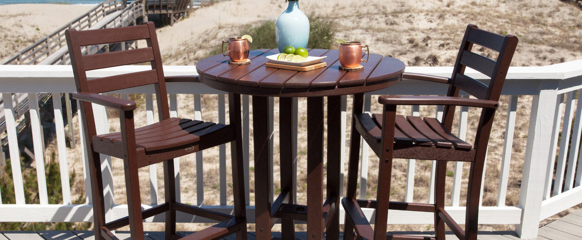 A brown Trex Outdoor Furniture Monterey Bay 3 Piece Bar Set sits before a white railing overlooking a sandy beach.