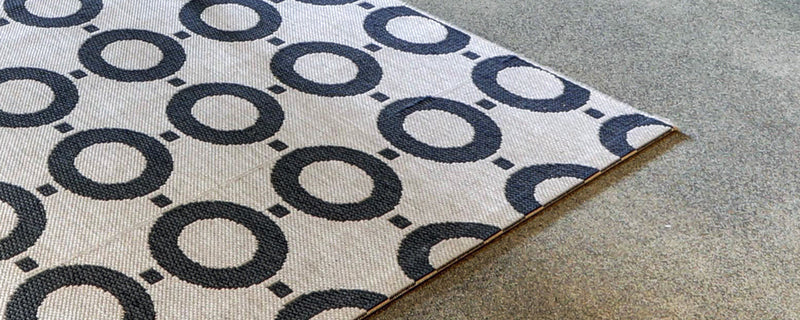 A white outdoor rug with black circles and dots lies on a concrete floor.