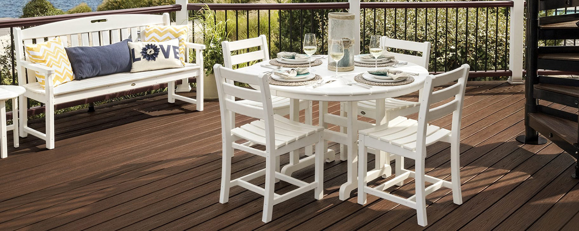 A white Trex Outdoor Furniture Monterey Bay 5 Piece Round Side Chair Dining Set sits on a brown composite deck.