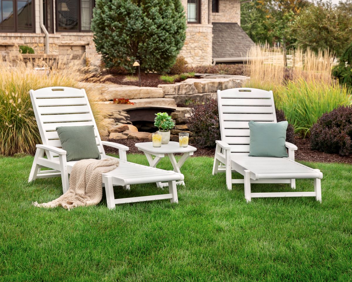 A white Trex Outdoor Furniture Yacht Club 3 Piece Chaise Set sits on a lawn before a brick house with landscaping.