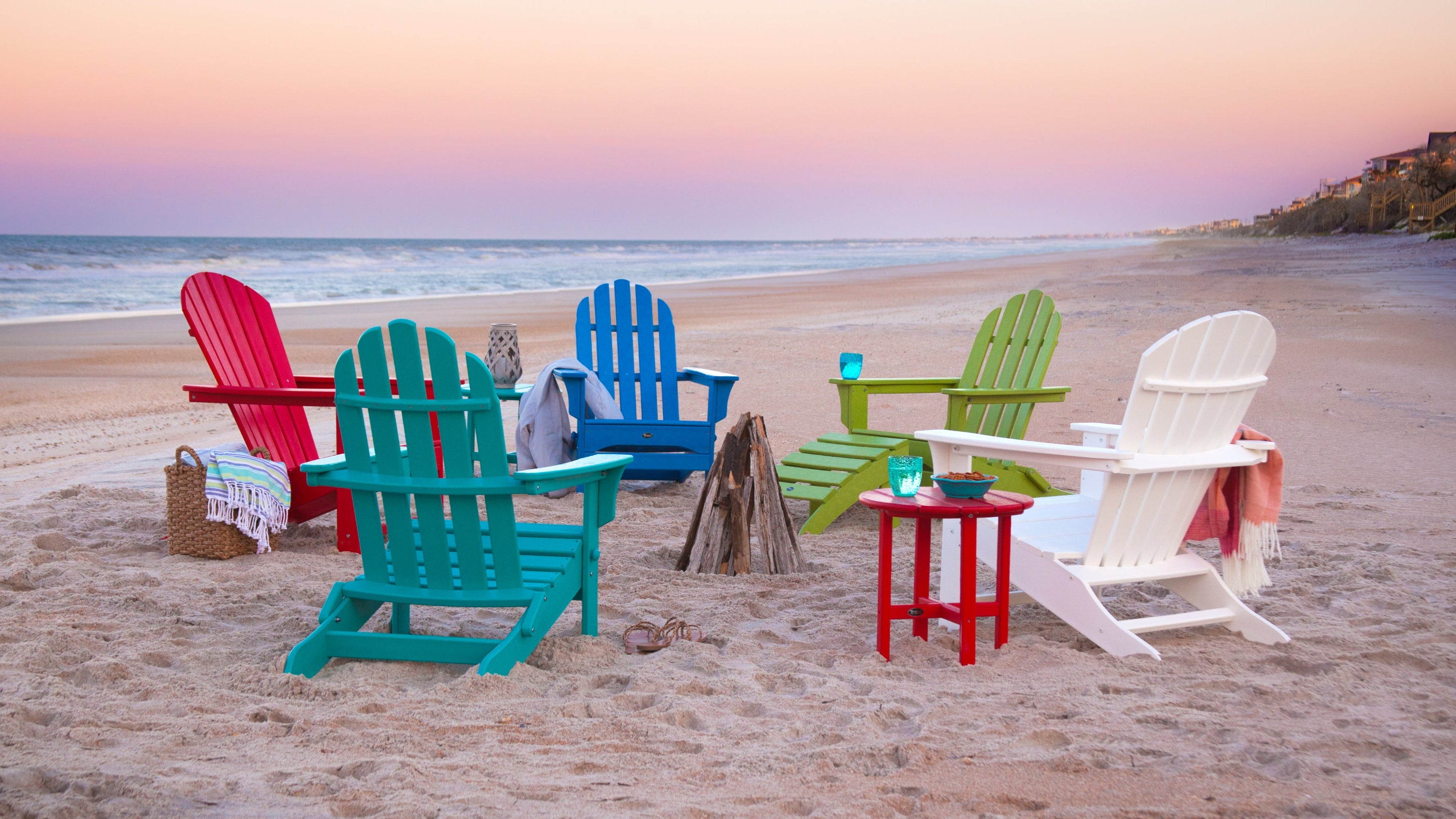 Colorful Trex Outdoor Furniture Adirondack chairs sit on a sandy beach with a sunset sky.