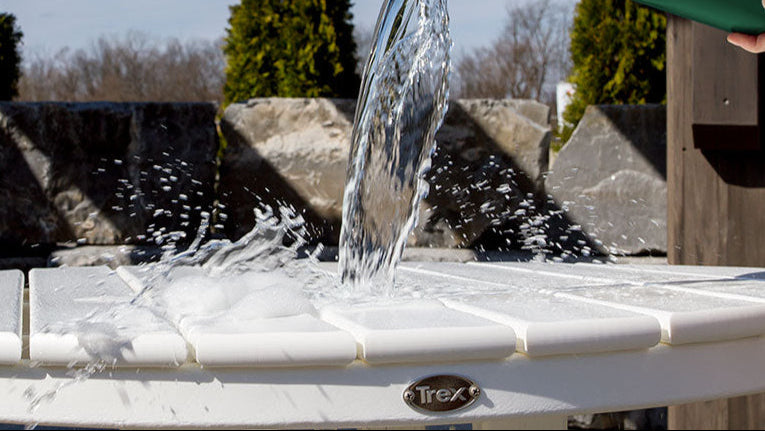 Water being poured from a green bucket onto a round white Trex Outdoor Furniture table.