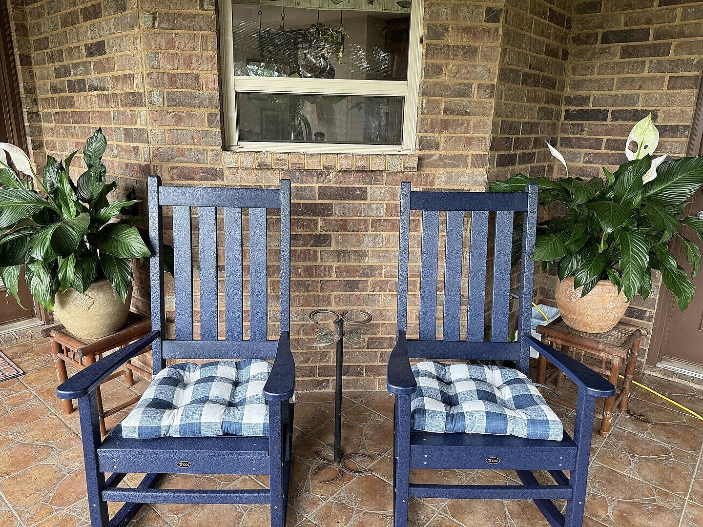 Two dark blue Trex Outdoor Furniture Cape Cod Porch Rocking Chairs sit on a patio by a brick house.
